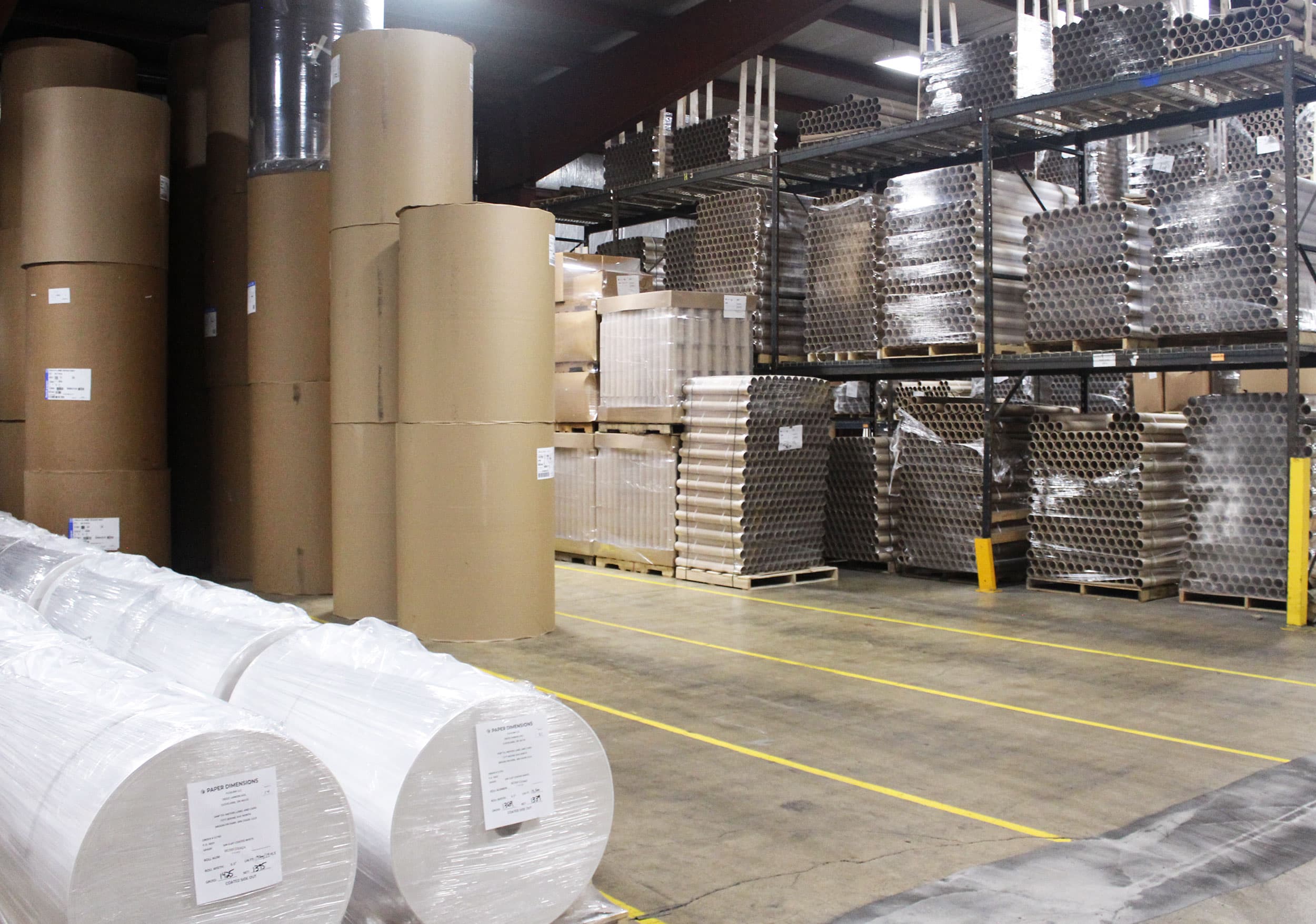 Parent paper rolls, racked paper cores, and wrapped finished rolls stored in the Paper Dimensions warehouse